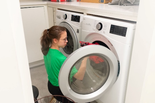 A person in a green shirt loading a washing machineDescription automatically generated